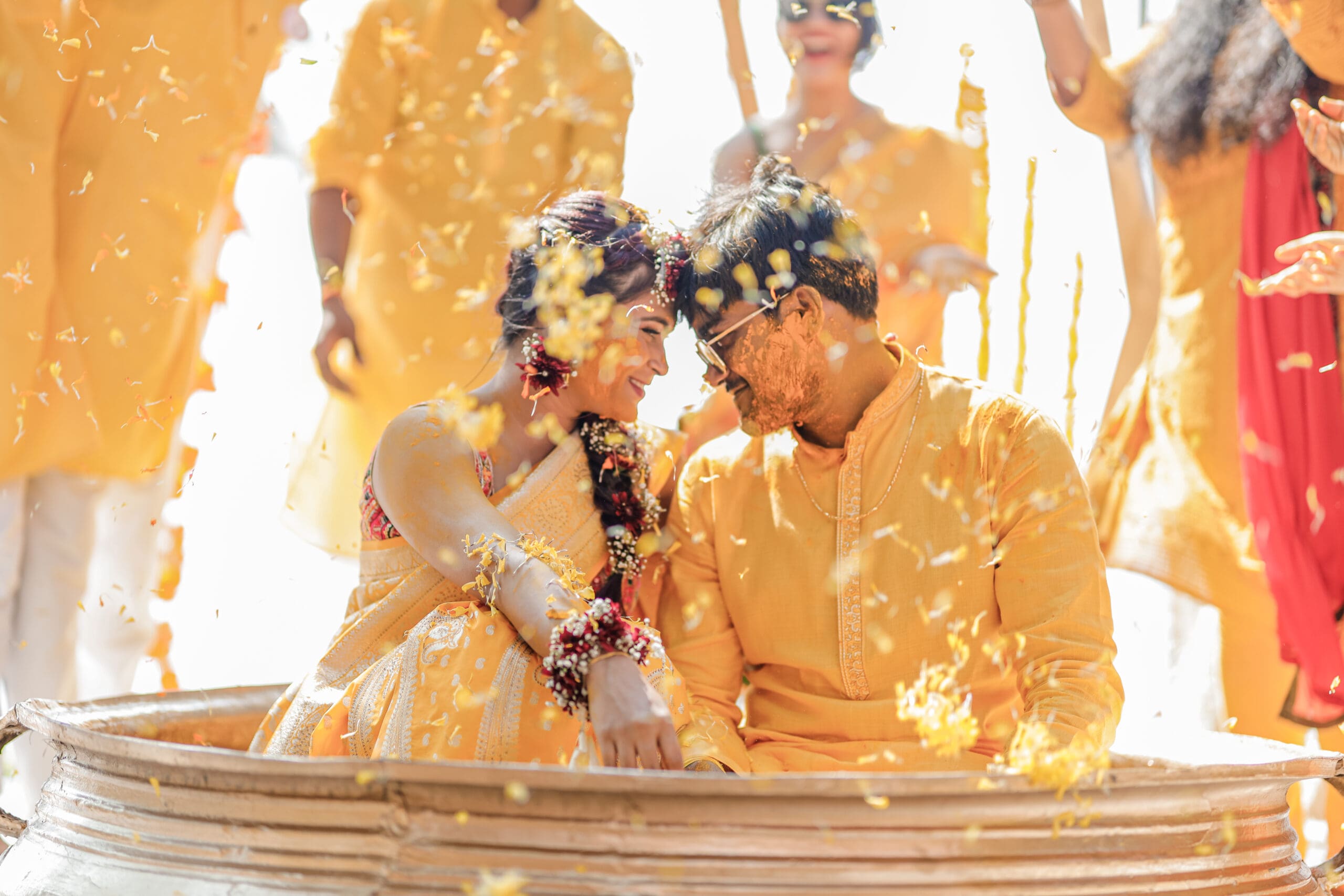 Bride and groom embrace the haldi traditions, sitting in a tub and touching heads.